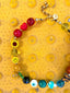 Lifestyle Image of Venessa Arizaga FW26 Over The Rainbow Necklace - A colorful statement beaded necklace with rainbow gradient charms including heart, flower, smiley, clover, eyeball, mushroom, butterfly, bead, and ladybug in ceramic, wood, and glass, on a textured yellow background