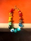 Lifestyle Image of Venessa Arizaga FW26 Over The Rainbow Necklace - A colorful statement beaded necklace with rainbow gradient charms including heart, flower, smiley, clover, eyeball, mushroom, butterfly, bead, and ladybug in ceramic, wood, and glass, on a subway seat