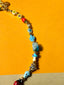 Venessa Arizaga FW26 Cosmic Roadtrip Necklace - A golden beaded necklace with classic icons - heart, smiley, alien, daisy, camera, clover, star - perfect for everyday layering, on a subway seat