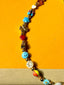 Venessa Arizaga FW26 Cosmic Roadtrip Necklace - A golden beaded necklace with classic icons - heart, smiley, alien, daisy, camera, clover, star - perfect for everyday layering, on a subway seat