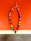 Lifestyle image of Venessa Arizaga FW26 Venus Heart Necklace (Rainbow) - A statement necklace with rainbow beads, pave accents, and a gold heart pendant, on a subway seat