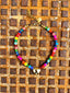 Lifestyle image of Venessa Arizaga FW26 Venus Heart Necklace (Rainbow) - A statement necklace with rainbow beads, pave accents, and a gold heart pendant, on a textured background.