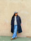 Model wearing a cap with 'NY' logo and Venessa Arizaga FW26 Talk of The Town Necklace - A statement gold beaded necklace with ceramic letter charms spelling "me", "you", "hi", "bye", "yes", "no", "omg" against a beige wall