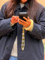 Model image of Venessa Arizaga FW26 Me Me Me Phone Leash - A statement gold beaded phone leash and bag charm with ceramic letter charms spelling "me", and Venessa Arizaga FW26 Talk of The Town Bracelet -  A statement three-row gold beaded elastic bracelet with ceramic letter charms spelling "xo", "luv", "me", "you", "hi", "bye", "yes", "no", "omg".