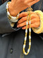 Close up model image of Venessa Arizaga FW26 Me Me Me Phone Leash - A statement gold beaded phone leash and bag charm with ceramic letter charms spelling "me", and Venessa Arizaga FW26 Talk of The Town Bracelet -  A statement three-row gold beaded elastic bracelet with ceramic letter charms spelling "xo", "luv", "me", "you", "hi", "bye", "yes", "no", "omg".
