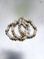Close up image of Venessa Arizaga FW26 Talk of The Town Bracelet -  A statement three-row gold beaded elastic bracelet with ceramic letter charms spelling "xo", "luv", "me", "you", "hi", "bye", "yes", "no", "omg". Three beaded bracelets with letter beads on a light gray background