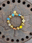 Lifestyle image of Venessa Arizaga FW26 Glitter Galaxy Bracelet - A golden beaded bracelet with classic icons - rainbow, smiley, butterfly, eyeball, mushroom, clover - perfect for everyday layering. Colorful beaded bracelet with gold beads and various charms on a rusted metal surface