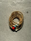 Lifestyle image of Venessa Arizaga FW26 Dreamwave Bracelet - Five rows of elastic gold beads and charms including a smiley face, ladybug, mushroom, alien, and star. Gold beaded bracelet with charms on a gray surface.