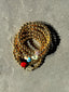 Lifestyle image of Venessa Arizaga FW26 Dreamwave Bracelet - Five rows of elastic gold beads and charms including a smiley face, ladybug, mushroom, alien, and star. Gold beaded bracelet with charms on a gray surface.