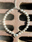 Lifestyle image of Venessa Arizaga FW26 Big Heart Necklace (Silver) - A silver beaded statement necklace with a large heart pendant. Silver beaded necklace with a heart charm on a textured surface.