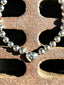 Lifestyle image of Venessa Arizaga FW26 Big Heart Necklace (Silver) - A silver beaded statement necklace with a large heart pendant. Silver beaded bracelet with a heart charm on a textured surface.