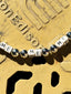 Lifestyle image of Venessa Arizaga FW26 Me Me Me Necklace (Silver) - A statement silver beaded necklace with ceramic letter charms spelling "me" on a textured gold surface.