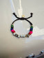 Lifestyle image of Venessa Arizaga FW26 Superstar Sparkle Bracelet - A statement adjustable bracelet with brown threadwork, pave accents, letter beads spelling SUPER, and a gold star charm. Colorful beaded bracelet with charms on a white surface.