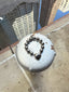 Lifestyle image of Venessa Arizaga FW26 Big Heart Bracelet (Silver) -  A silver beaded elastic statement bracelet with a large heart pendant. Silver beaded bracelet on a metal post with a cityscape background.