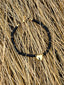 Lifestyle image of Venessa Arizaga FW26 Venus Heart Necklace (Black) - A statement necklace with black glass beads, pave accents, and a gold heart pendant. Black beaded bracelet with a gold heart-shaped clasp on a sandy surface with dry grass.
