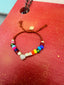 Lifestyle image of Venessa Arizaga FW26 Love Spark Bracelet - adjustable beaded bracelet with rust threadwork, pave accents, and letter beads spelling LOVE with a heart charm. Colorful beaded bracelet on a red surface.