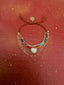 Lifestyle image of Venessa Arizaga FW26 Sweetheart Sparkle Bracelet (Rainbow) - A layered bracelet with rust threadwork, rainbow seed beads, gold plated chains, rhinestone chain, and a pave heart charm. Multistrand beaded bracelet with heart charm on a red textured background.