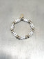 Lifestyle image of Venessa Arizaga FW26 Me Me Me Bracelet (Silver) -  An everyday silver elastic beaded bracelet with ceramic letter charms spelling "me" on a metallic surface