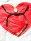 Lifestyle image of Venessa Arizaga FW26 Twinkle Bracelet - An everyday adjustable multi-layer bracelet with brown threadwork, rainbow seed beads, gold-plated chains, and a pavé star charm. Multicolored beaded bracelet with a gold charm on a red heart-shaped fabric.