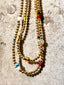 Lifestyle image of Venessa Arizaga FW26 Dreamwave Necklace - Two rows of gold beads and playful charms including a smiley face, ladybug, mushroom, alien, and star on a textured surface.