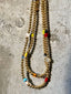 Lifestyle image of Venessa Arizaga FW26 Dreamwave Necklace - Two rows of gold beads and playful charms including a smiley face, ladybug, mushroom, alien, and star on a textured surface.