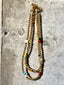 Lifestyle image of Venessa Arizaga FW26 Dreamwave Necklace - Two rows of gold beads and playful charms including a smiley face, ladybug, mushroom, alien, and star on a textured surface.