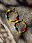 Lifestyle image of Venessa Arizaga FW26 Dreamwave Earrings - hoop earrings with gold beads and dangling butterfly, mushroom, and smiley charms on a textured stone surface