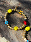 Lifestyle image of Venessa Arizaga FW26 Dreamwave Earrings - hoop earrings with gold beads and dangling butterfly, mushroom, and smiley charms on a textured stone surface