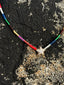 Lifestyle image of Venessa Arizaga FW26 Twinkle Necklace - An everyday adjustable necklace with brown threadwork, rainbow seed beads, and a pavé star charm on a textured surface