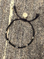 Lifestyle image of Venessa Arizaga FW26 Lover Bracelet - An everyday adjustable bracelet with black threadwork, black glass seed beads, and rhinestone heart charms on a textured stone surface
