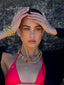 Model image of Venessa Arizaga FW26 Dreamwave Necklace - Two rows of gold beads and playful charms including a smiley face, ladybug, mushroom, alien, and star and the Dreamwave Bracelet - Five rows of elastic gold beads and charms including a smiley face, ladybug, mushroom, alien, and star . Model in colorful outfit standing against a textured wall.