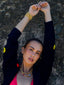 Model image of Venessa Arizaga FW26 Dreamwave Necklace - Two rows of gold beads and playful charms including a smiley face, ladybug, mushroom, alien, and star and the Dreamwave Bracelet - Five rows of elastic gold beads and charms including a smiley face, ladybug, mushroom, alien, and star . Model in colorful outfit standing against a textured wall.