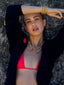Model image of Venessa Arizaga FW26 Dreamwave Necklace - Two rows of gold beads and playful charms including a smiley face, ladybug, mushroom, alien, and star and the Dreamwave Bracelet - Five rows of elastic gold beads and charms including a smiley face, ladybug, mushroom, alien, and star . Model in colorful outfit standing against a textured wall.