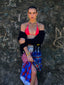 Model image of Venessa Arizaga FW26 Dreamwave Necklace - Two rows of gold beads and playful charms including a smiley face, ladybug, mushroom, alien, and star, the Dreamwave Bracelet - Five rows of elastic gold beads and charms including a smiley face, ladybug, mushroom, alien, and star, and Dreamwave Earrings - hoop earrings with gold beads and dangling butterfly, mushroom, and smiley charms . Model in colorful outfit standing against a textured wall.