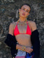 Model image of Venessa Arizaga FW26 Dreamwave Necklace - Two rows of gold beads and playful charms including a smiley face, ladybug, mushroom, alien, and star, the Dreamwave Bracelet - Five rows of elastic gold beads and charms including a smiley face, ladybug, mushroom, alien, and star, and Dreamwave Earrings - hoop earrings with gold beads and dangling butterfly, mushroom, and smiley charms . Model in colorful outfit standing against a textured wall.