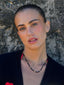 Close-up model image of Venessa Arizaga FW26 Lover Necklace - An everyday adjustable necklace with black threadwork, black glass seed beads, and sparkling rhinestone heart charms. Model wearing a black cardigan with a textured wall background