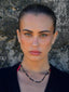 Close-up model image of Venessa Arizaga FW26 Lover Necklace - An everyday adjustable necklace with black threadwork, black glass seed beads, and sparkling rhinestone heart charms. Model wearing a black cardigan with a textured wall background