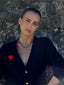 Close-up model image of Venessa Arizaga FW26 Lover Necklace - An everyday adjustable necklace with black threadwork, black glass seed beads, and sparkling rhinestone heart charms. Model wearing a black cardigan with a textured wall background