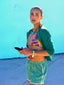 Model image of Venessa Arizaga FW26 Over The Rainbow Necklace & Bracelet - A colorful beaded statement necklace and bracelet with rainbow gradient charms including heart, flower, smiley, clover, eyeball, mushroom, butterfly, bead, and ladybug in ceramic, wood, and glass, and Over The Rainbow Phone Leash, a statement multi use phone accessory and bag charm with iconic charms in rainbow hues.