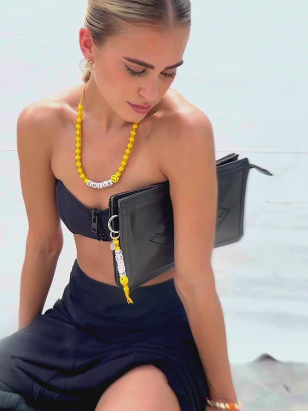 Close up Video of Sugar Rush Smile multi-function keychain and bag charm by Venessa Arizaga shown on a clutch, with yellow threadwork, glass and ceramic charms, and a joyful smiley motif. Styled with the Sugar Rush Happy necklace in adjustable leather cord and yellow glass charms and ceramic smile charms.